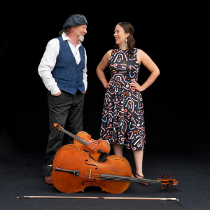 white male in cap and white female in patterned dress laughing about their fiddle and cello