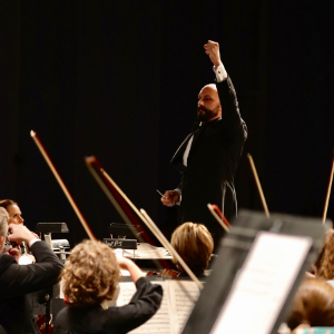 conductor in tuxedo raised arm leading orchestra