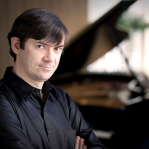 Pianist Dmitri Vorobriev wearing a black shirt with a slightly blurry piano in the background.