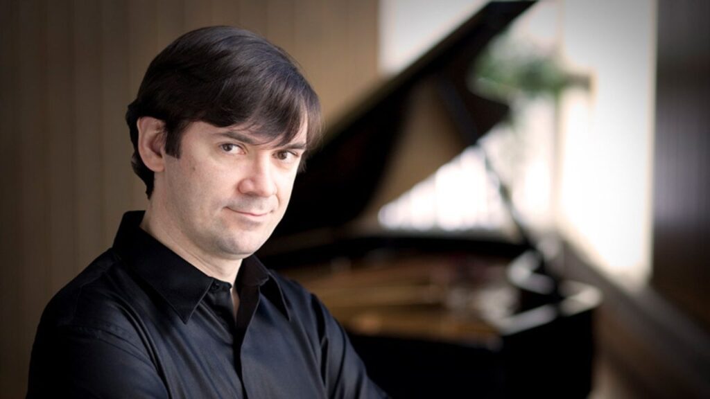 Pianist Dmitri Vorobriev wearing a black shirt with a slightly blurry piano in the background.