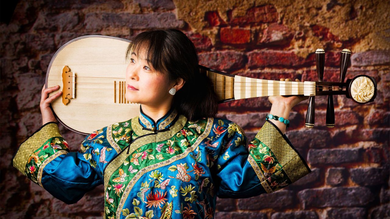 Asian female in traditional gown holds a pipa, a Chinese lute, on shoulders.