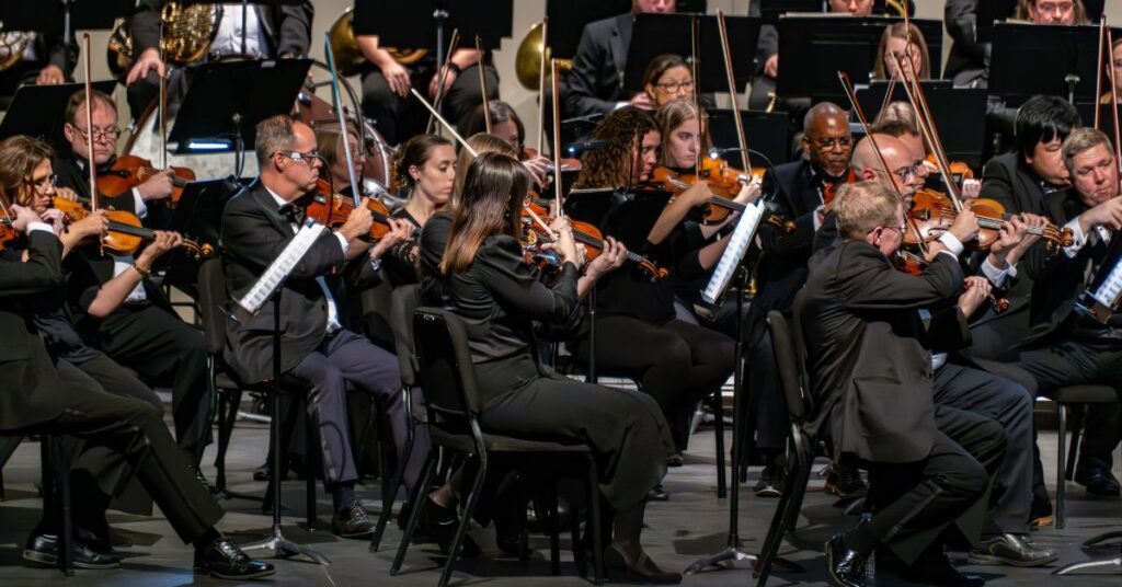 group of orchestra violin musicians playing together wearing all back clothes and holding violins