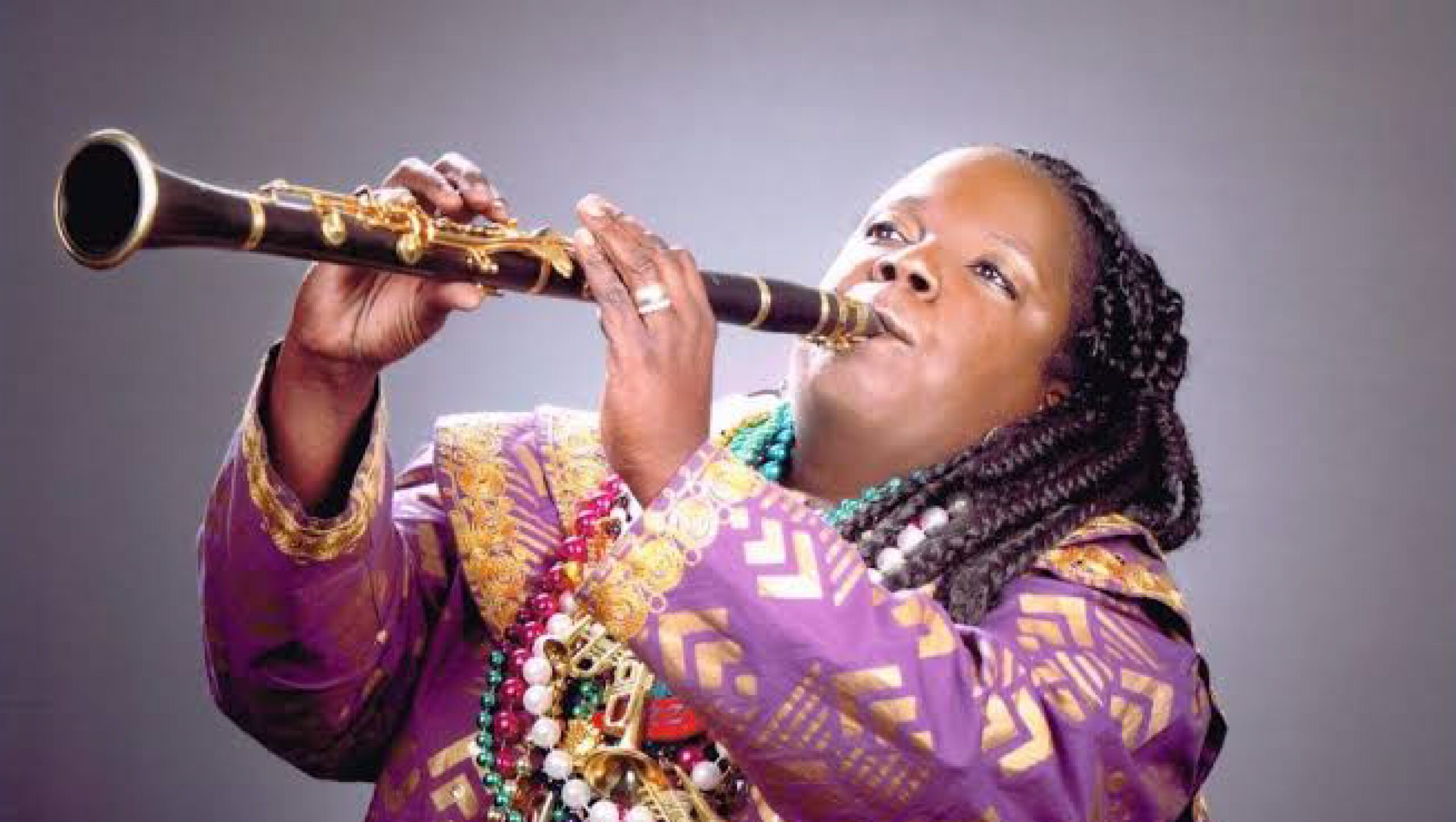 a black woman playing a clarinet and wearing purple green gold NOLA jacket