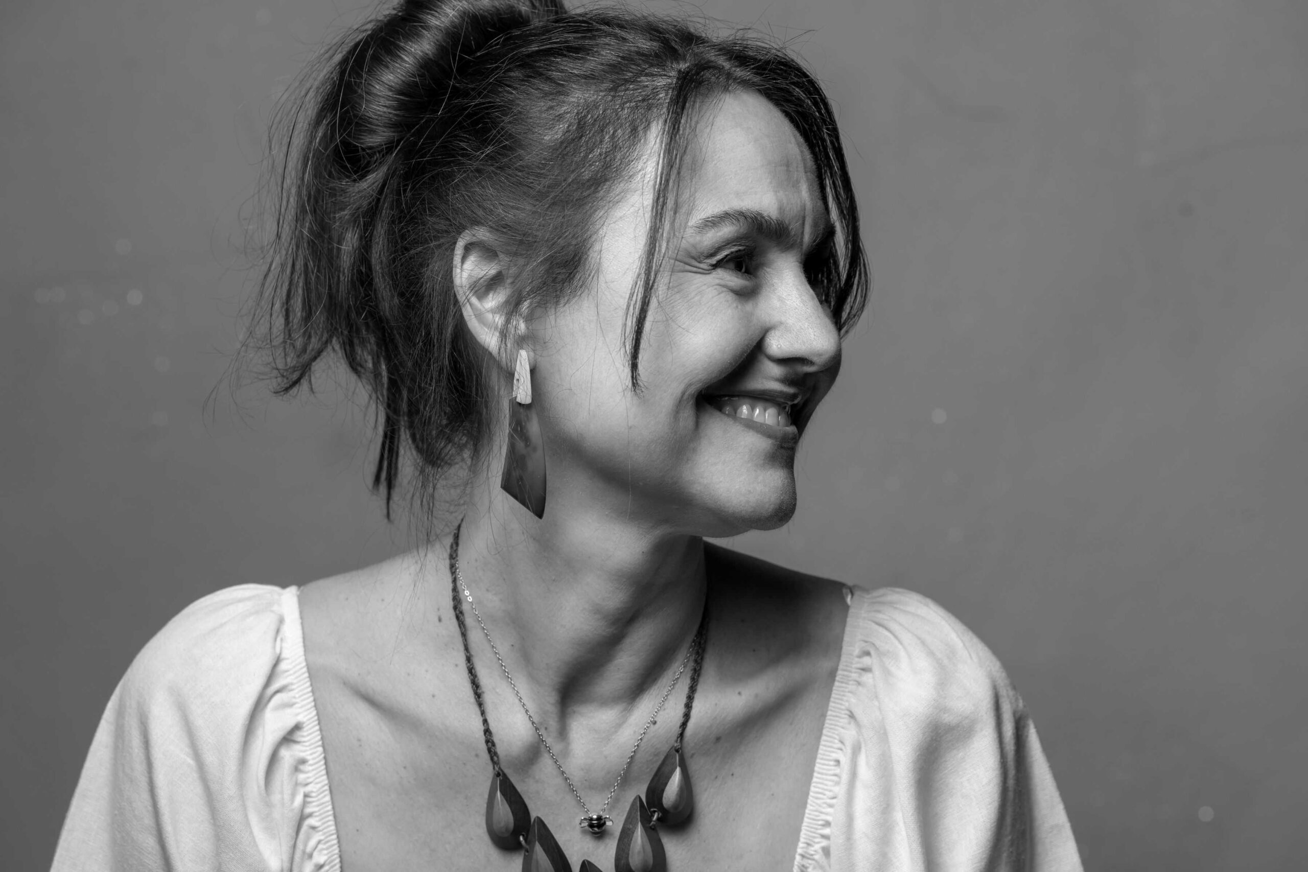 black and white photo of white femail in white blouse with wooden necklace and wooden earrings black hari in a messy ponytail and looking to the right