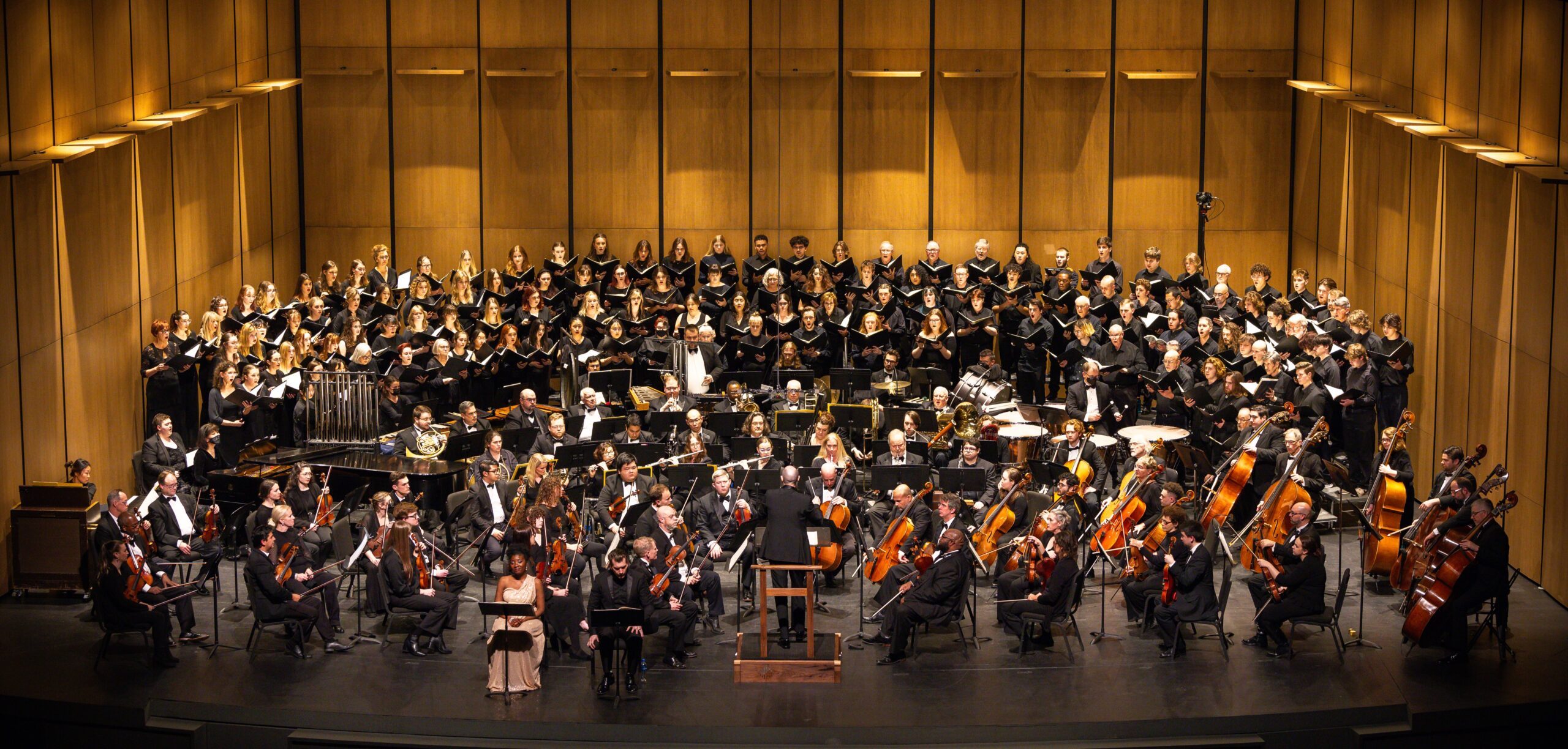 large orchestra with one hundred chorus singers and three solo singers in the front, everyone wearing formal black and white outfits