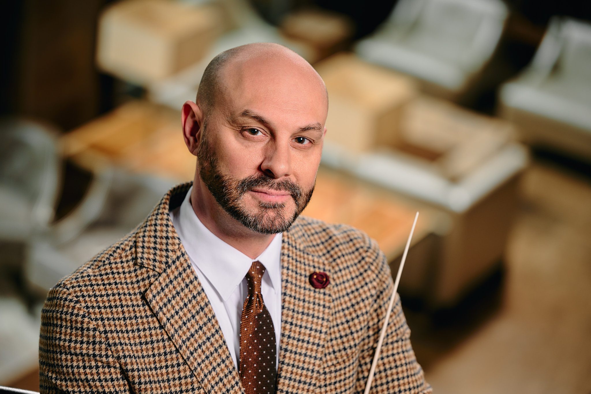 white male with braodn beard and bald hear wearing a tweed jacket and holding a conductor's baton while smilling at the camer